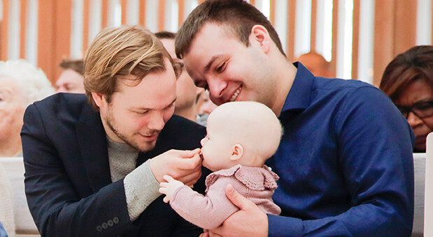 To unge mænd sidder med baby i kirken før barndåb