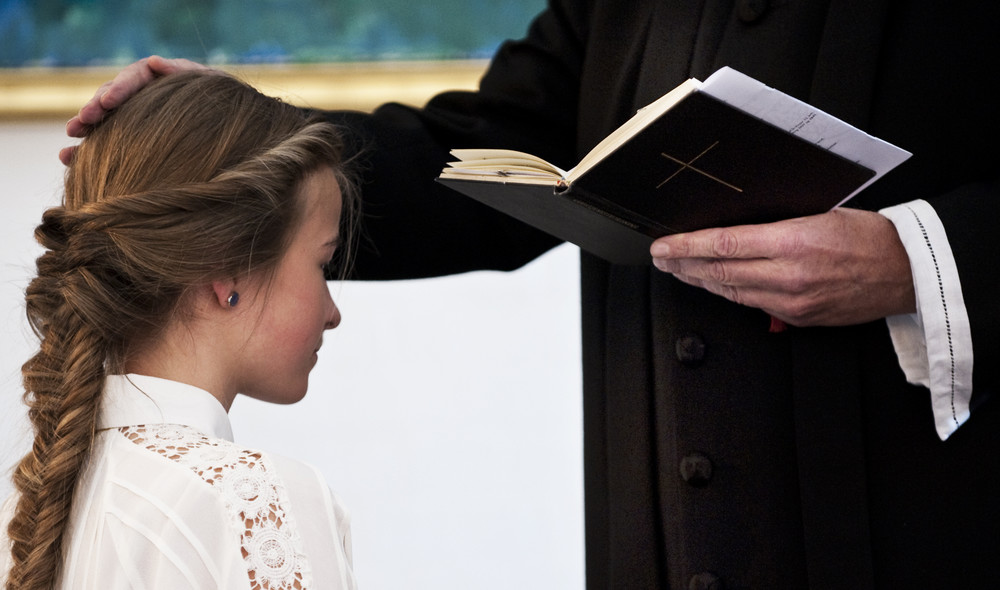 Præst lægger hånd på hovedet af konfirmand ved konfirmation i folkekirken
