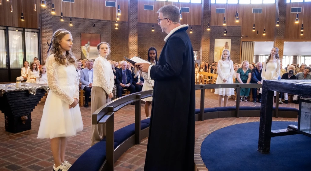 5 konfirmander står foran knæfaldet i kirken og lytter opmærksomt til præsten .