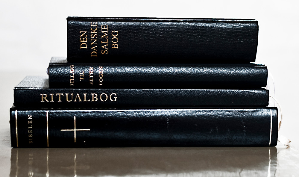 Bibel, Ritualbog og Salmebog indbundet i sort læder med guldtryk ligger i bunke på alter folkekirkens liturgier