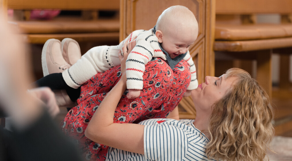 Mor leger med sin baby på gulvet i en kirke til babysalmesang