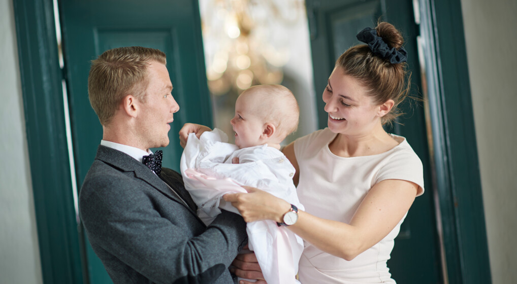 Forældre giver barn dåbskjole på før barnedåb i kirken 