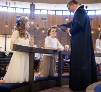 En pige knæler ved knæfaldet, imens præsten er ved at konfirmere hende.