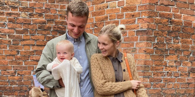 Et ungt forældrepar står med et dåbsbarn foran kirken og smiler til barnet